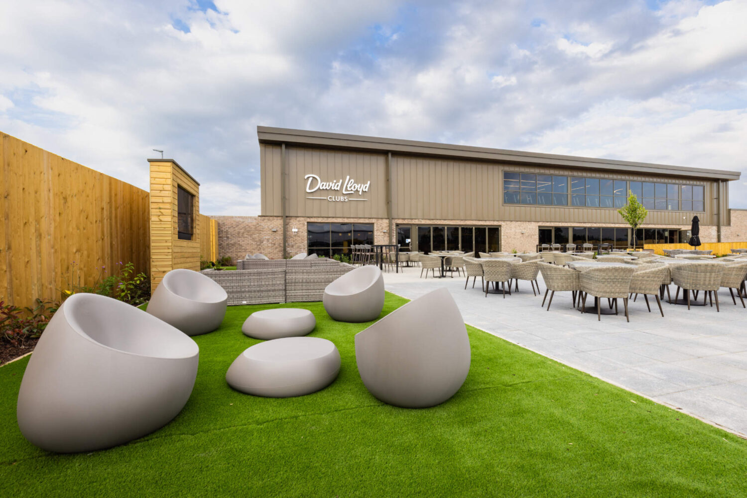 David Lloyd Clubs outdoor patio featuring round grey chairs on artificial grass and a paved dining area.