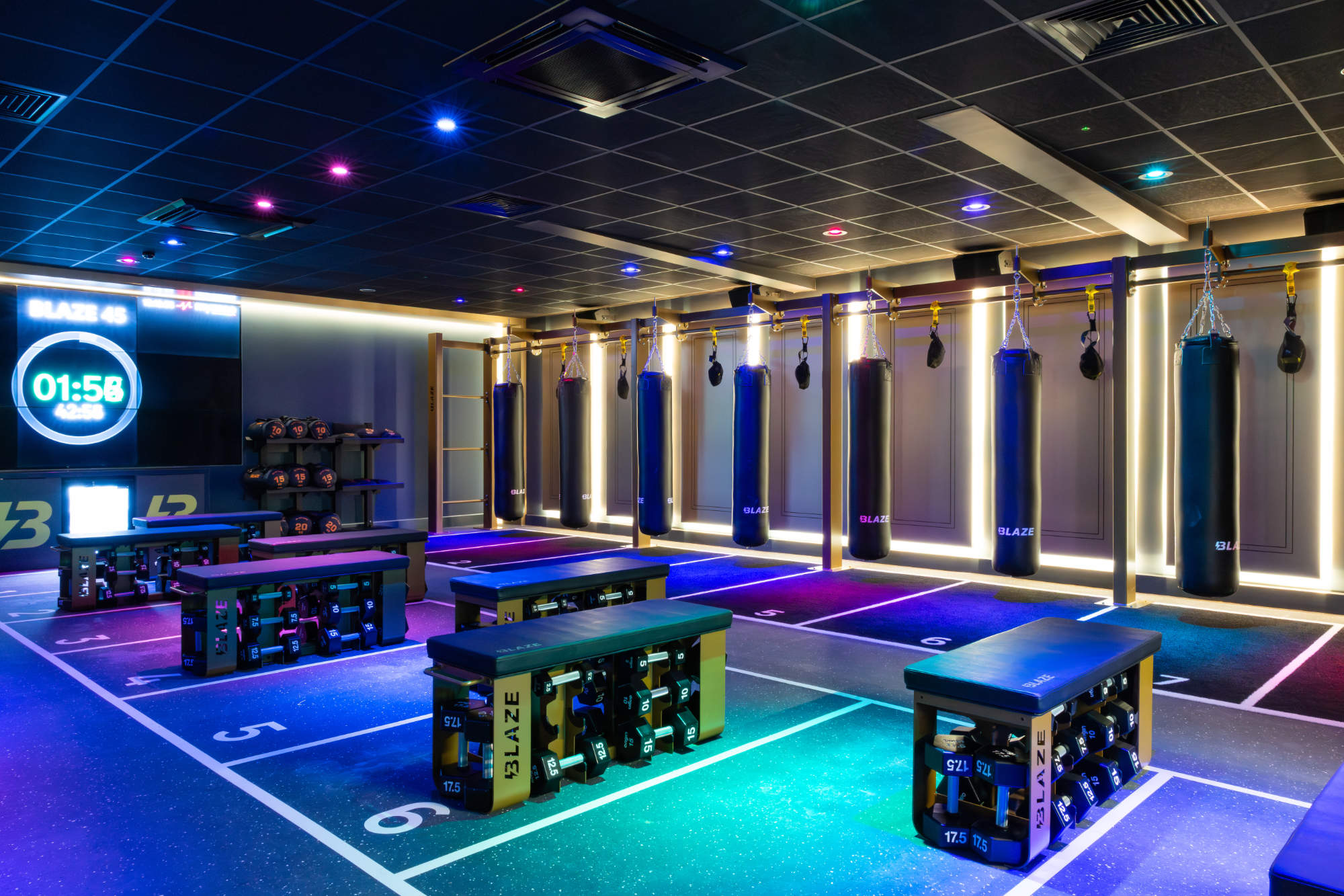 Neon-lit fitness studio with black punching bags and workout benches storing dumbbells on a numbered blue floor.